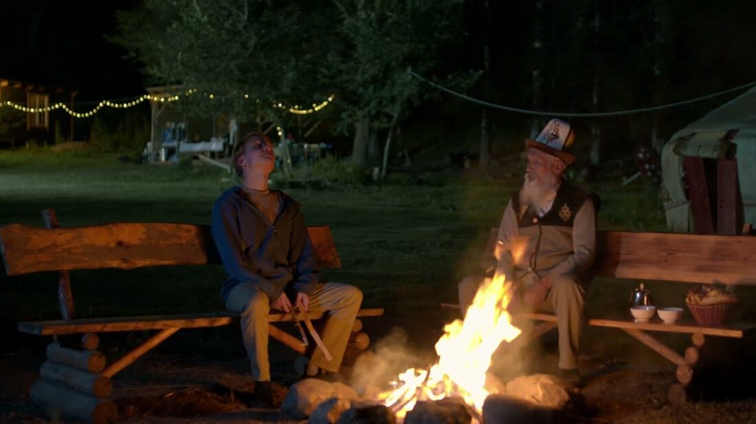 Live-action still — Alex and Bakai by the campfire at night